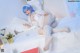 A woman with blue hair is sitting on a bed.