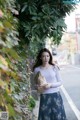 A woman standing on the side of a road holding a brown paper bag.